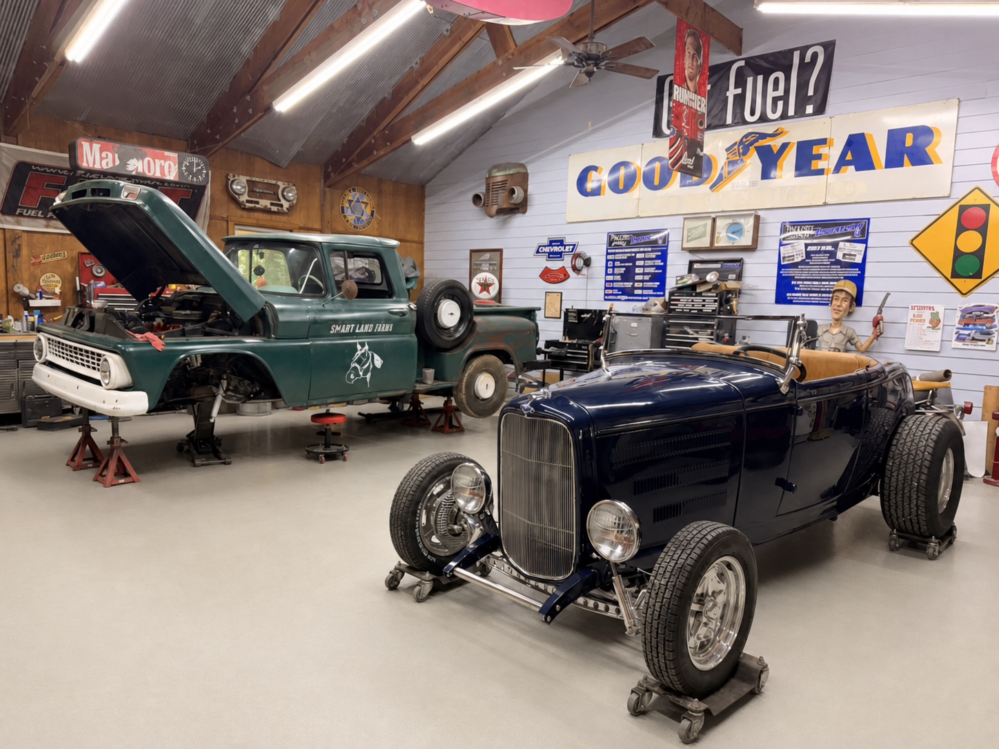 Nightmist Blue 1932 Ford Roadster displayed inside a professional hot rod workshop beside a vintage Chevrolet truck